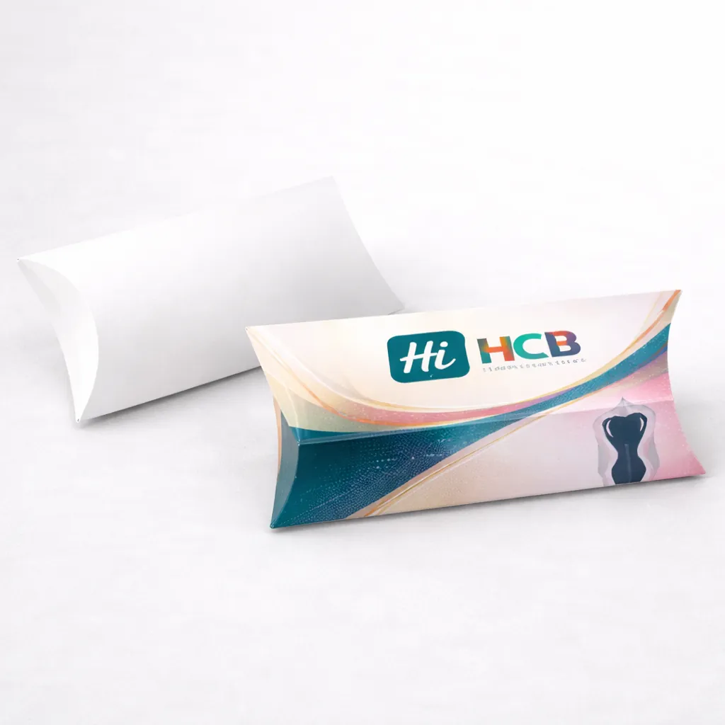 A white pillow-shaped box beside a custom-printed version with a teal logo and a shaper silhouette. class=